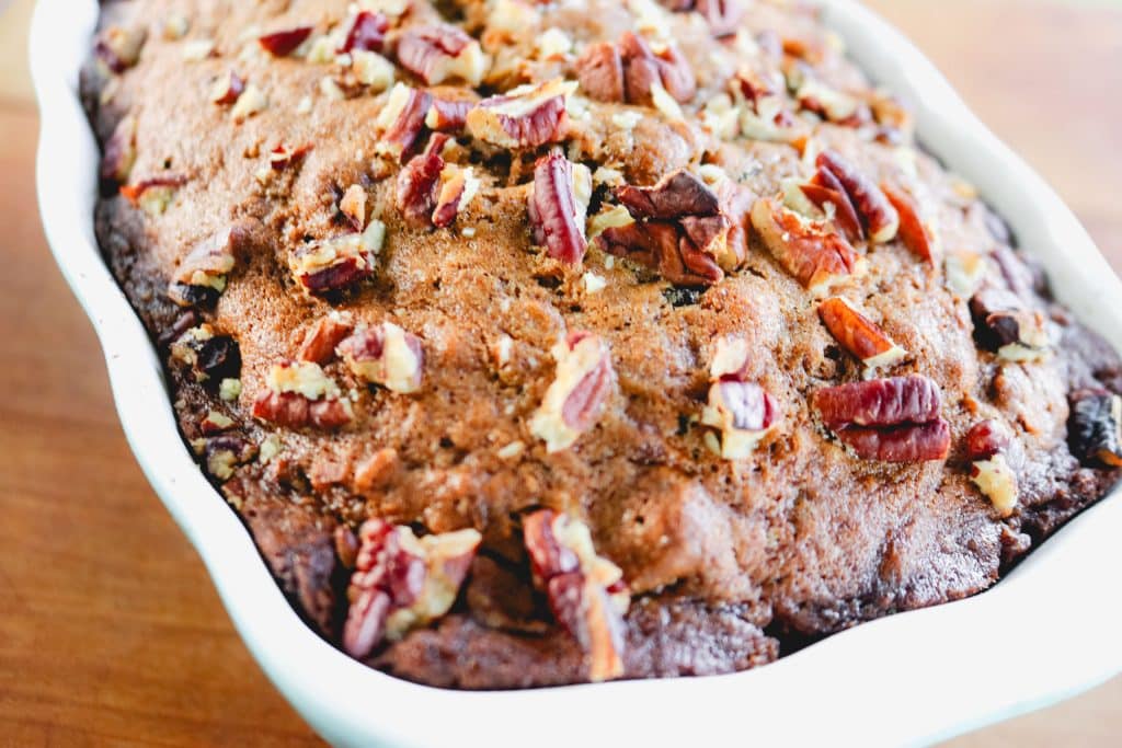 the top of zucchini bread with pecans in a white loaf pan on a wood counter