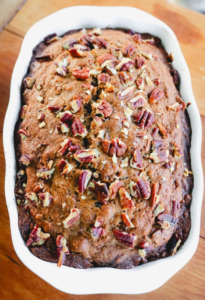zucchini bread with pecans on top in a loaf pan on a wood counter