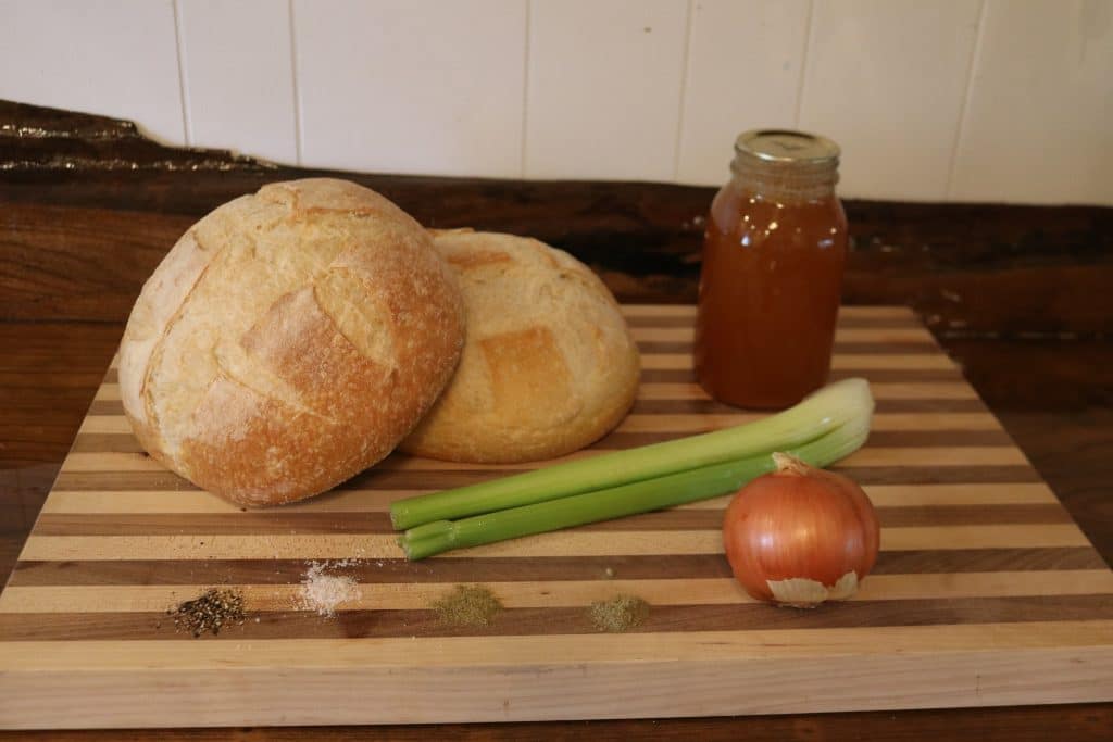 two bread loaves, broth, celery. onion and seasonings on a cutting board 