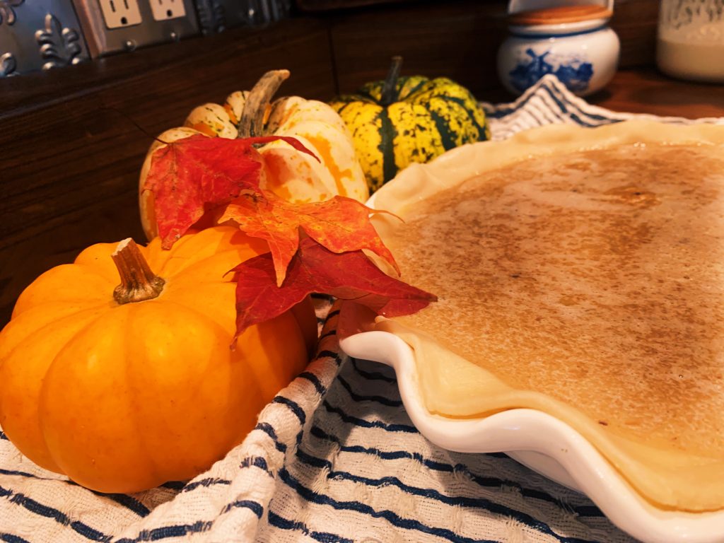 pumpkins and leaves on a towel beside an uncooked pumpkin pie