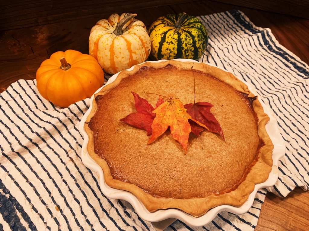 Pumpkin pie with leaves on top of pie and pumpkins around the pie on a white and black tea towel