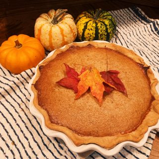 Pumpkin pie with leaves on top of pie and pumpkins around the pie on a white and black tea towel