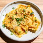 a white plate of lobster ravioli with butter sauce, chives and parmesan