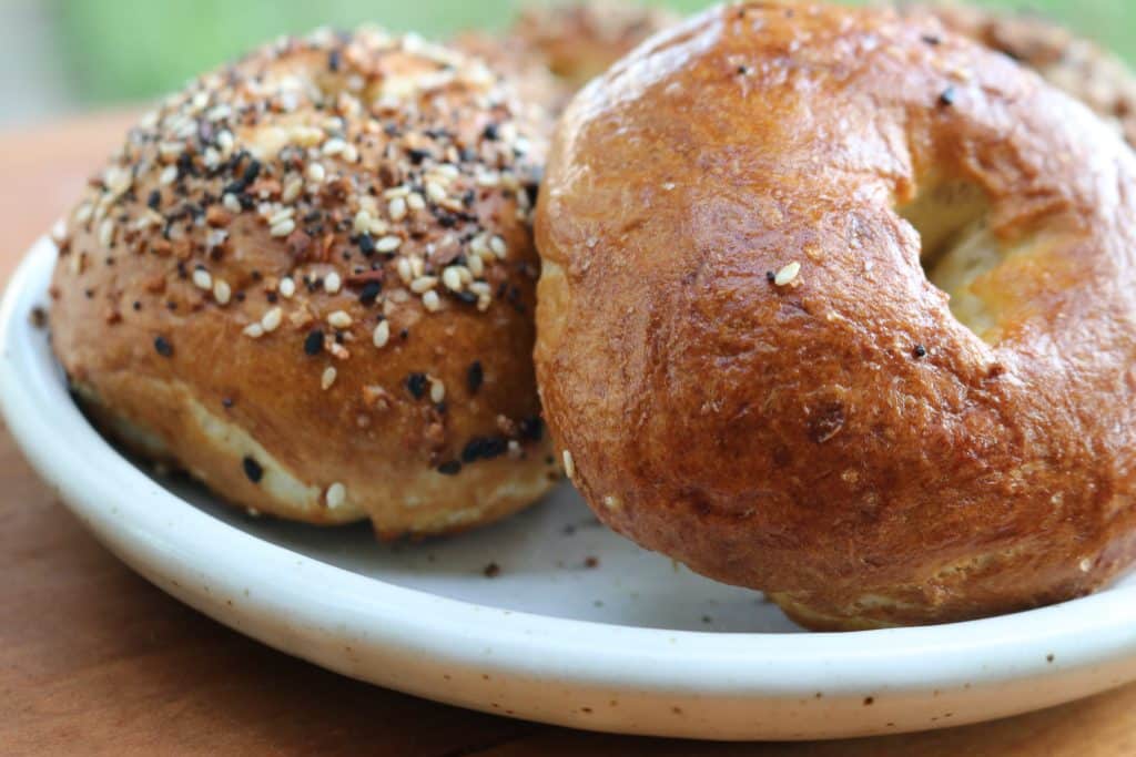 two bagels on a white plate, one with everything bagel seasoning and one plain.