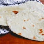 white flour tortillas on top of a black and white tea towel on a counter