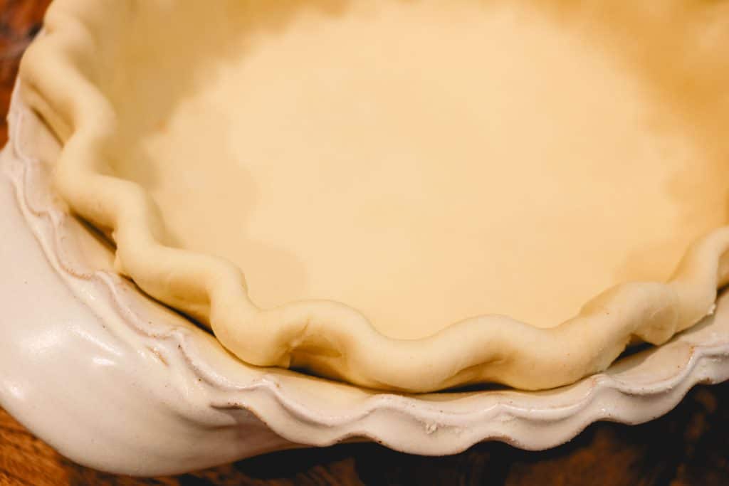 fluted edge of an unbaked pie crust in a white pie dish